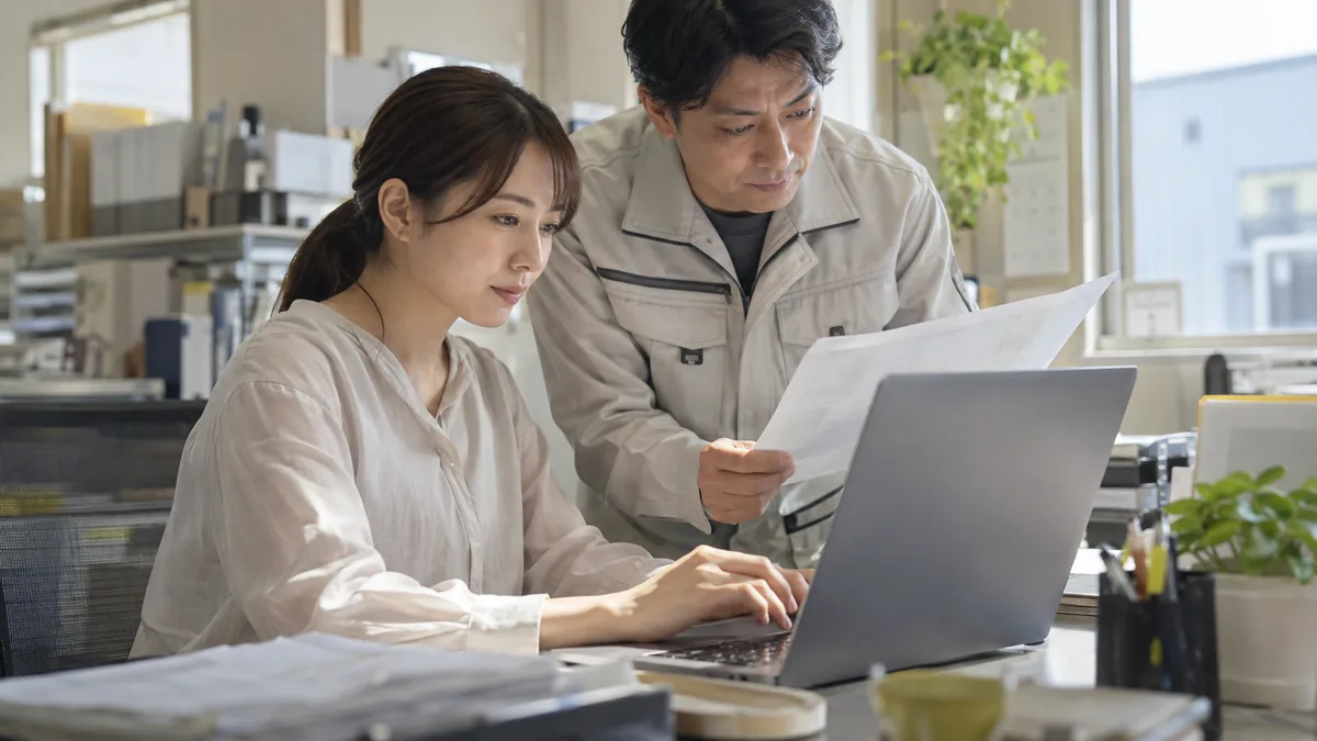 社員がパソコンで作成した資料を同僚と確認するイメージ